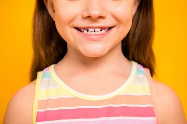 Cropped photo of charming kid having toothy smile wearing tank-top isolated over yellow background