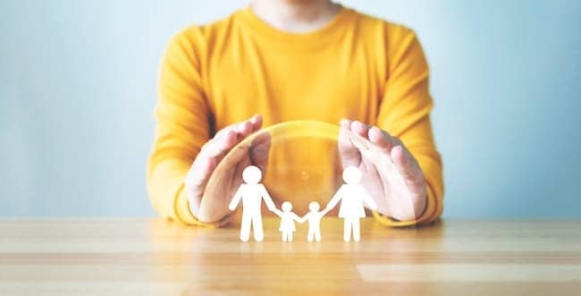 Hand protecting family on wood table. Healthcare and life insurance concept