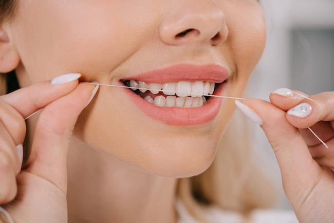 Partial view of woman flossing teeth with dental floss